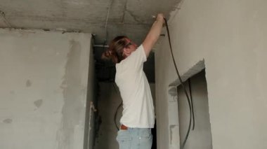 Renovation apartment. Electrical wiring. Empty walls, repairs house with their own hands. Man electrician installing laying electrical cables with pliers inside the house under construction. 