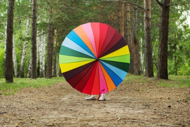 Happy funny girl holding rainbow umbrella. Cute Happy schoolgirl playing in rainy summer park. Kid walking in autumn shower. Outdoor fun by any weather.