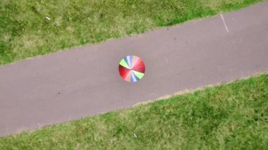 Aerial dron view. Top view. Man with a colorful umbrella in park. Positive young people using rainbow umbrella and flag during the rain in the park. LGBTQ concept