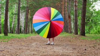 Happy funny girl holding rainbow umbrella. Cute Happy schoolgirl playing in rainy summer park. Kid walking in autumn shower. Outdoor fun by any weather.