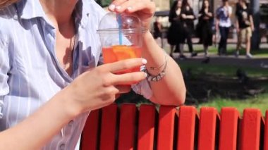 Aperol sprey kokteyli, yakın çekim. Plastik bardakta yaz içkisi. Bir kızın ellerinde canlandırıcı alkollü içecek.