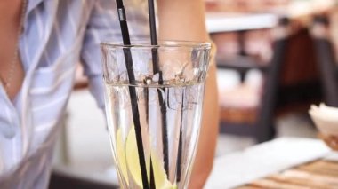 Bir kız yaz terasında bir kafede kokteyl içiyor, yakın plan. Limonlu ve buzlu yaz içeceği. Ferahlatıcı alkollü içecek.