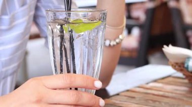 Bir kız yaz terasında bir kafede kokteyl içiyor, yakın plan. Limonlu ve buzlu yaz içeceği. Ferahlatıcı alkollü içecek.