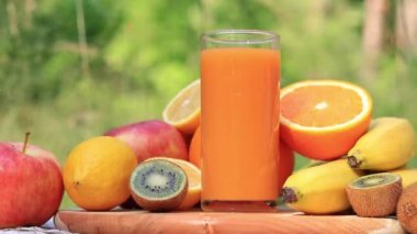 Bir kadının eli bir bardak multivitamin suyu alır. Olgun meyveler, doğanın arka planına karşı bir bardağın etrafına serilmiştir. Reklam sıvıları, vitaminler ve sağlıklı yaşam tarzı videoları