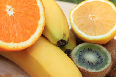 Muz, portakal, limon ve kividen oluşan olgun meyveler, yakın fotoğraf. Meyve bileşimi, bazıları ikiye bölünmüş.