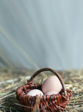 Eggs in a small wicker basket stand on hay, blurred background. Vertical background for Easter holiday