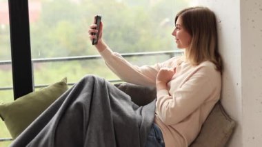 Kız, arkadaşları ya da ailesi ile telefon kamerasıyla iletişim kuruyor. Belli bir mesafeden internet üzerinden iletişim. Pencerenin dışında sonbahar yağmurlu havası, battaniyeli bir kız. Evde kal.