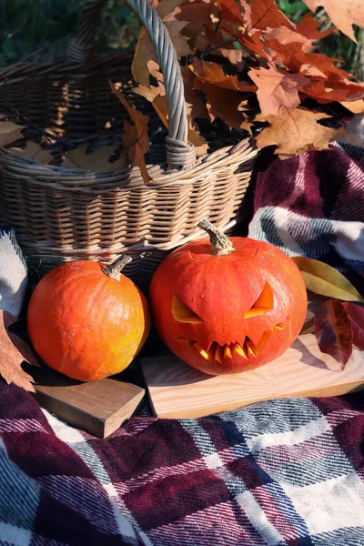 A pumpkin with a carved Halloween face near a basket on a plaid. Halloween concept, terrifyingly face on a pumpkin