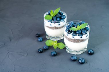 Koyu arkaplanda taze toplanmış yaban mersini, yoğurt ve chia tohumlarıyla tabakta hafif ve sağlıklı bir tatlı. Diyet kahvaltı. Bu bir kayıp. Metin için yer.
