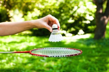 Parkta güneşli bir günde badminton oynamak için elinde raket ve mekikle dolaşan genç bir kadın eli. Yakın plan. Sağlıklı yaşam tarzını kabul et. Fitness konsepti.