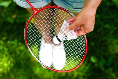 Güneşli bir günde parkta kadın eli, raketin üstünde servis aletini tutuyor. Badminton oynuyorum. Sağlıklı yaşam tarzı kavramı. Fitness konsepti. Yakın plan..