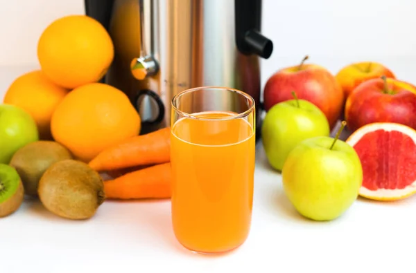 A glass of freshly squeezed fruit juice, fruit and a modern juicer on the table in the kitchen. Homemade healthy fruit and vegetable juices. Selective focus. Close-up.