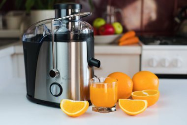 Modern meyve sıkacağı, bir bardak taze portakal suyu ve portakallar mutfaktaki masada. Doğal ve sağlıklı sıvılar. Yakın plan..