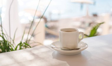 Güneşli bir yaz gününde kumsaldaki kafede terasta beyaz bir fincan kahve. Yakın plan. Uzayı kopyala Seçici odak.