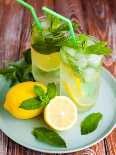 Doğal ferahlatıcı limonata ile iki bardak ya da limonlu mojito kokteyli, naneli ve buzlu. Ahşap zemin üzerinde soğuk yaz içeceği. Yakın plan..