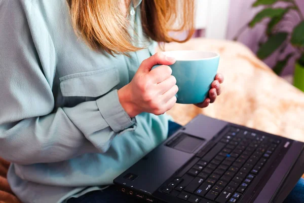 Çay içen ve evde dizüstü bilgisayarla çalışan genç bir kadın. Çevrimiçi öğrenme. Yakın plan..