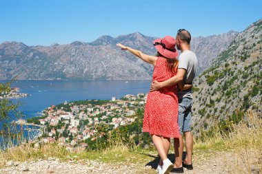 Sevgi dolu bir çift güneşli bir yaz gününde yüksek bir dağdan güzel bir deniz manzarası izler. Kadın uzaktaki bir şeyi gösteriyor. Tatil ve seyahat konsepti. Boşluğu kopyala.