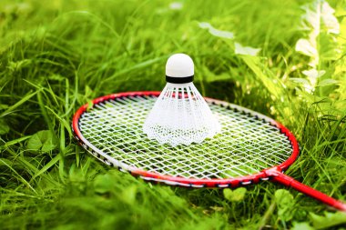 Beyaz mekikli horoz ve badminton raketi yeşil çimlerin üzerinde yatıyor. Parlak yaz güneşli bir gün. Sağlıklı yaşam tarzını kabul et. Fitness konsepti.