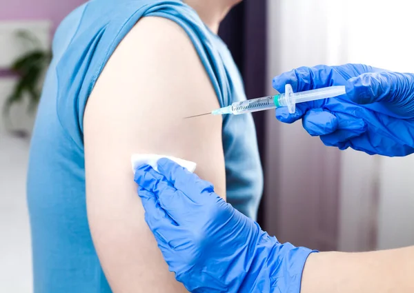 Mavi lastik koruyucu eldivenli bir doktor erkek hastaya iğne ya da aşı yapar. Sağlık hizmetleri. Grip ve koronavirüs aşısı. Yakın plan..