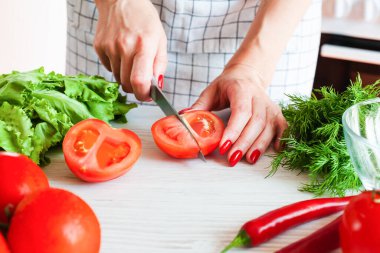 Bıçaklı bir kadın eli taze olgun bir domatesi tahta beyaz tahtada keser. Sağlıklı gıda konsepti. Yakın plan..