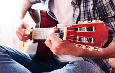 Kareli gömlekli genç adam gitar çalıyor. Yakın plan..
