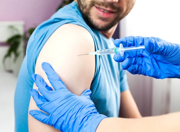 Influenza and coronavirus vaccination. A doctor in blue rubber protective gloves makes an injection or vaccination to young man. Health care. Close-up.