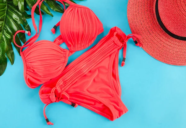 Kırmızı kadın mayosu, kırmızı şapka ve mavi arka planda yeşil palmiye dalları. Düz yatıyordu. Üst görünüm.