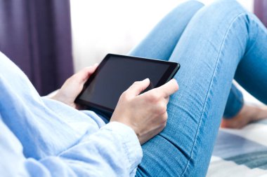 Genç bir kız evde yatakta otururken tablet üzerinde çalışır. Evde çalış, çalış, online alışveriş yap..