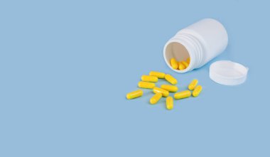 Mavi arka plandaki şişeden yayılmış sarı haplar. Tıp konsepti. Uzayı kopyala Yakın plan..