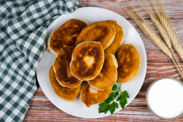 Hot fried homemade pies on the plate and sour cream on a wooden table. Top view. Close-up.