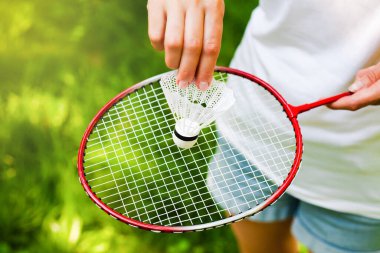 Güneşli bir günde parkta kadın eli, raketin üstünde servis aletini tutuyor. Badminton oynuyorum. Sağlıklı yaşam tarzı kavramı. Fitness konsepti. Yakın plan..