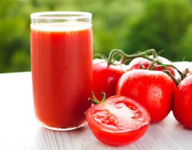 Bir bardak taze soğuk domates suyu ve ahşap beyaz arka planda olgun domatesler. Yakın plan..