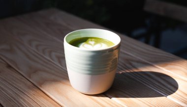 Cafe 'deki ahşap masada bir fincan yeşil çay, matcha latte. Güneşli bir gün. Sağlıklı gıda konsepti. Yakın plan. Boşluğu kopyala.