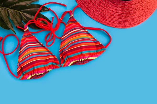 Women\'s red swimsuit and red hat flatlay composition on blue background. Top view. Place for text.