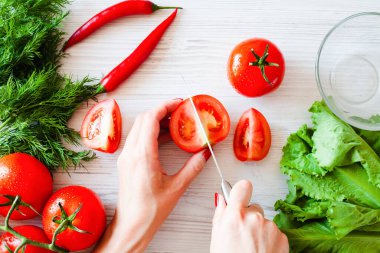 Bıçaklı kadın eller taze olgun bir domatesi tahta beyaz tahtada keser. Olgun sebzeli taze salata hazırlıyorum. Sağlıklı gıda konsepti. Yakın plan. Üst görünüm.