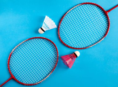 Mavi arka planda badminton oynamak için iki raket ve iki mekik horozu olan bir spor dairesi. Sağlıklı yaşam tarzını kabul et. Üst görünüm.