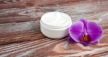 Yüz kremi kavanozu ve orkide, ahşap arka planda. Doğal cilt bakım ürünleri. Yakın plan. Boşluğu kopyala.
