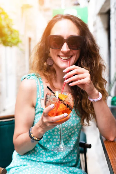 Gülümseyen genç kız soğuk bir kokteyl içer ve bir yaz sokak kafesinde dinlenir. Yaz. Tatilde. Seçici odak.