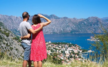 Genç aşık çift yüksek bir dağdan güzel bir deniz manzarasının tadını çıkarıyor. Güneşli bir yaz günü. Tatil ve seyahat konsepti. Mesaj için yer. Seçici odak.