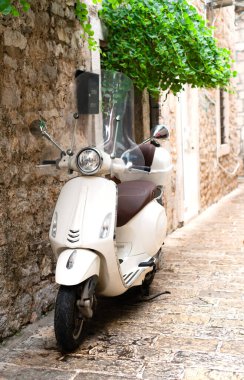Eski kasabanın caddesinde park edilmiş klasik beyaz scooter. Eğlence, seyahat, tatil. Seçici odak.