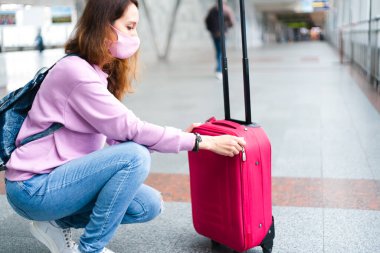 Sırt çantalı ve koruyucu maskeli genç kız valizi havaalanında ya da tren istasyonunda kapatıyor. İyi yolculuklar. Uzayı kopyala Seçici odak.