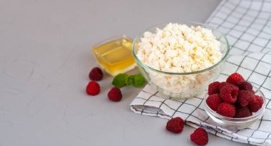 Süzme peynir, taze ahududu ve gri arka planda bal. Sağlıklı ve lezzetli bir kahvaltı. Yakın plan. Boşluğu kopyala.