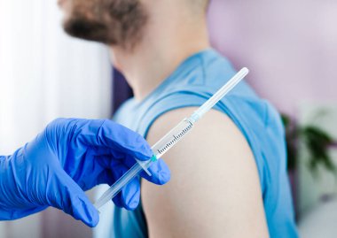 Plastik koruyucu eldivenli bir doktor erkek hastaya iğne ya da aşı yapar. Sağlık hizmetleri. Aşı, aşı, Covid-19 tedavisi. Yakın plan..