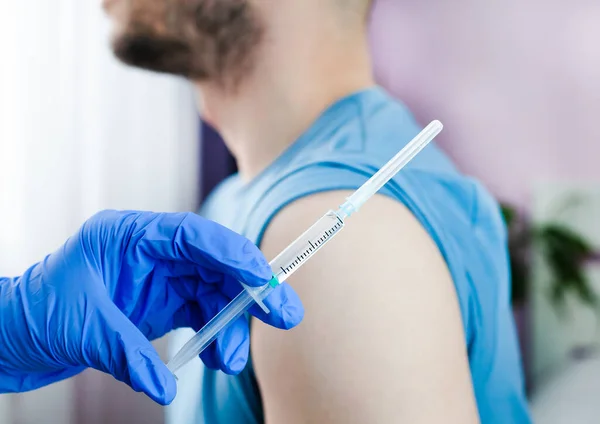 A doctor in rubber protective gloves makes an injection or vaccination to male patient. Health care. Vaccination, immunization, treatment to Covid-19. Close-up.