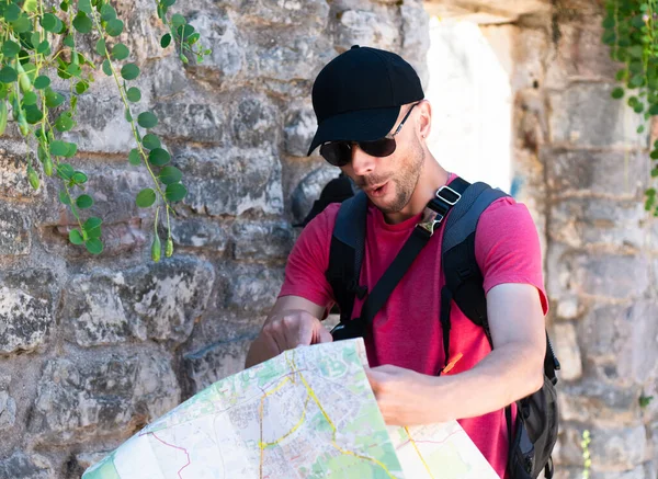 Surprised and joyful male tourist found the metho on the map and pointing at it with his finger. A man walks around the old city and sees the sights. Selective focus.