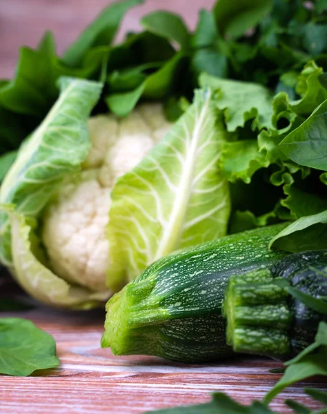 Zucchini, cauliflower and a variety of green leafy vegetables on a wooden background. Close-up. Selective focus.