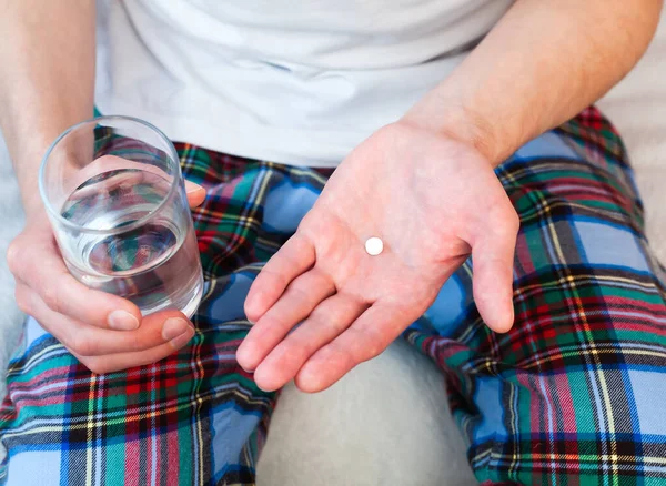 Young man holds one pill and glass of water in hands. Taking antibiotic, antidepressant, painkiller medication. Close-up.