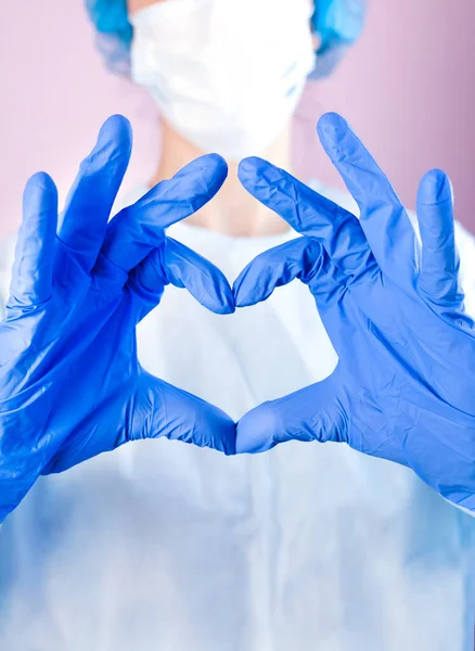 Doctor or nurse in medical mask and hands in protective gloves shows the symbol of the heart. Love, care and safety symbol. Doctor care and love concept to patients. Close-up.