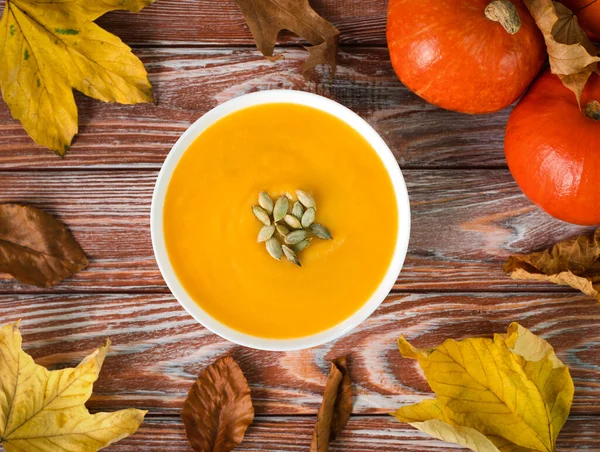 Pumpkin soup, autumn leaves and pumpkins on a wooden background. Top view.