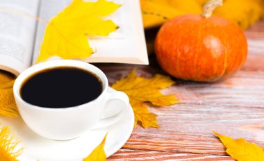 Hello, Autumn. Autumn composition with cup of hot coffee, pumpkin and a book on wooden background. Close-up. Copy space. Selective focus.